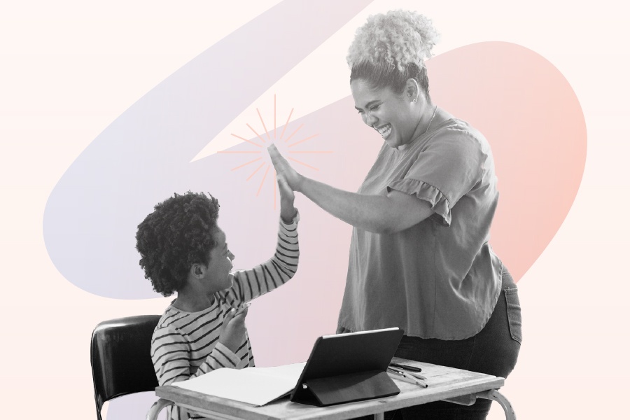 Educator giving a high five to elementary school student seated at desk.